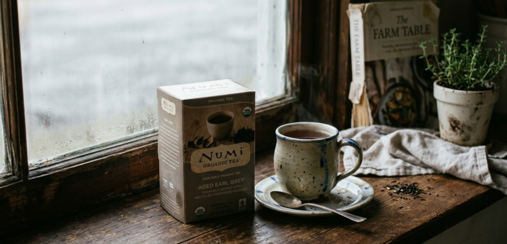 Numi organic loose leaf tea pouch next to a ceramic mug on a linen cloth in natural light